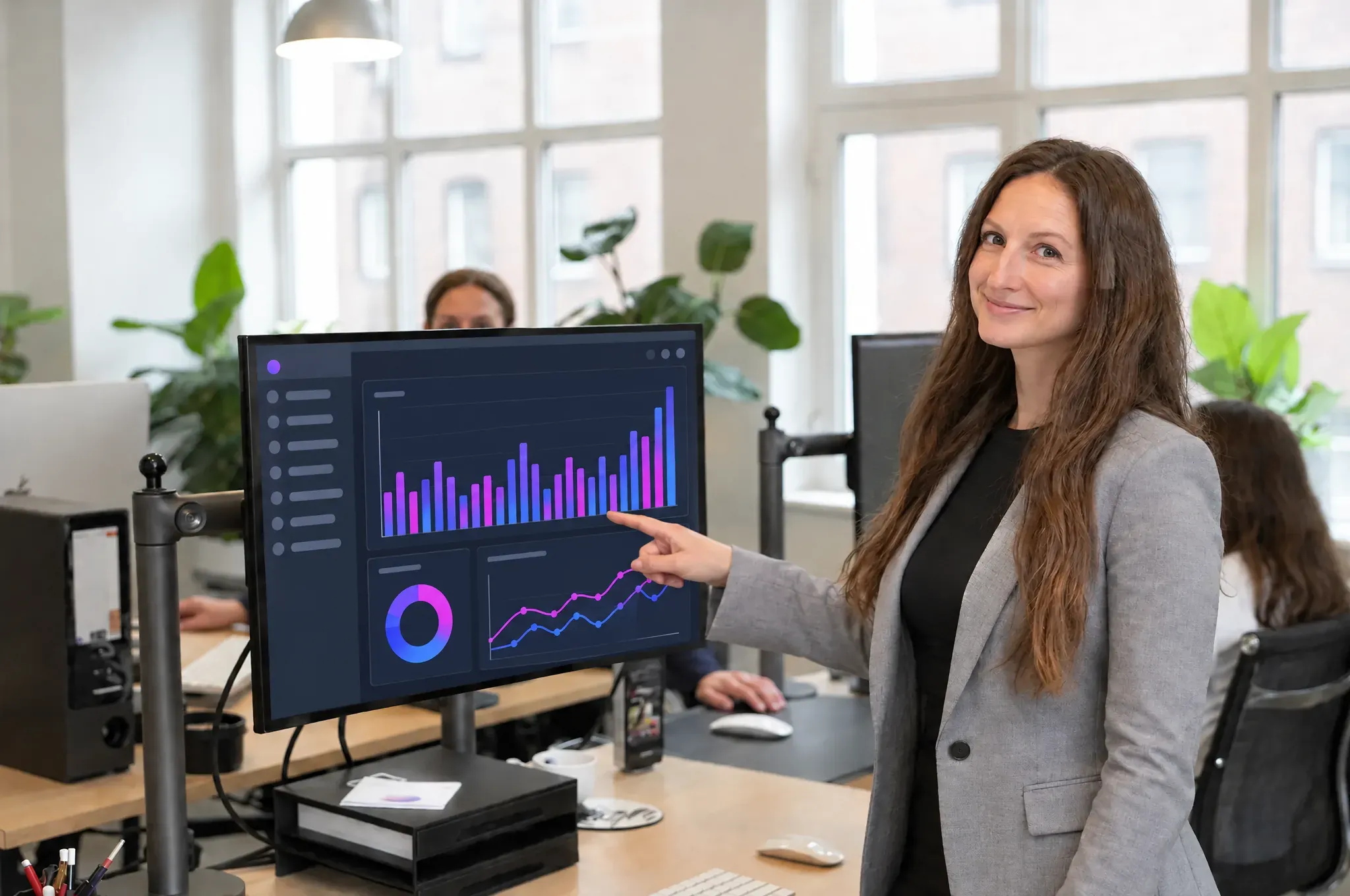 Nadine Fraiss zeigt im Büro einer Softwarefirma auf einen Monitor mit einem farbigen Dashboard.